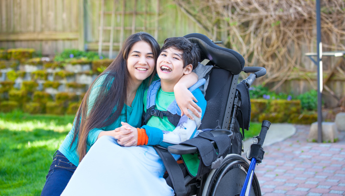 Image of young boy in paediatric wheelchair being hugged by family member or carer.